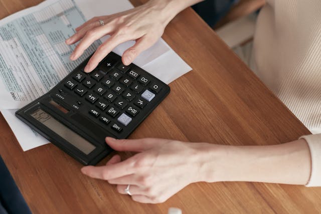 a-person-using-a-black-calculator-on-a-wooden-table-with-tax-documents-and-envelopes-nearby